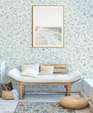 Wooden bench with white cushions against a floral wallpaper wall.