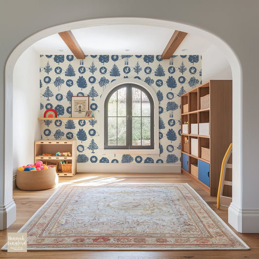 A room with white walls covered in a blue and brown nature-themed wallpaper featuring hand-drawn illustrations of trees and leaves. The room also has wooden furniture and a patterned area rug.