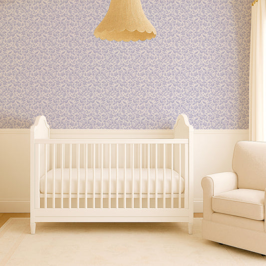 Nursery room with a white crib and beige chair against a patterned wall.
