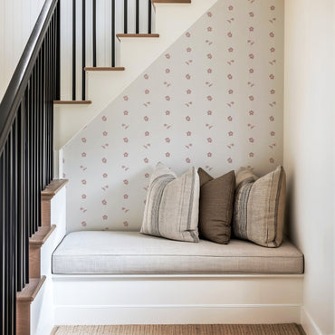 Nook with cushions against a wall with floral wallpaper, next to a staircase.
