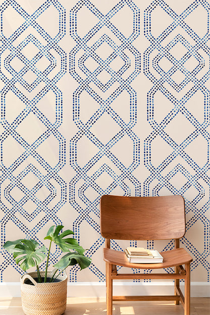 Blue and cream geometric patterned wallpaper shown in a styled room setting with a wooden chair and a potted plant.