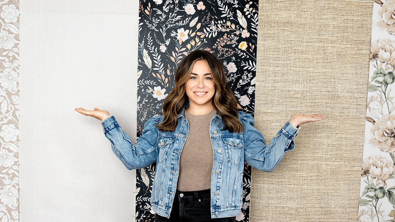 A woman stands with her arms outstretched between four vertical fabric or wallpaper swatches in different patterns and colors: beige floral, solid white, black floral, and tan linen.