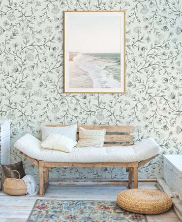 Wooden bench with white cushions against a floral wallpaper wall with a framed picture.