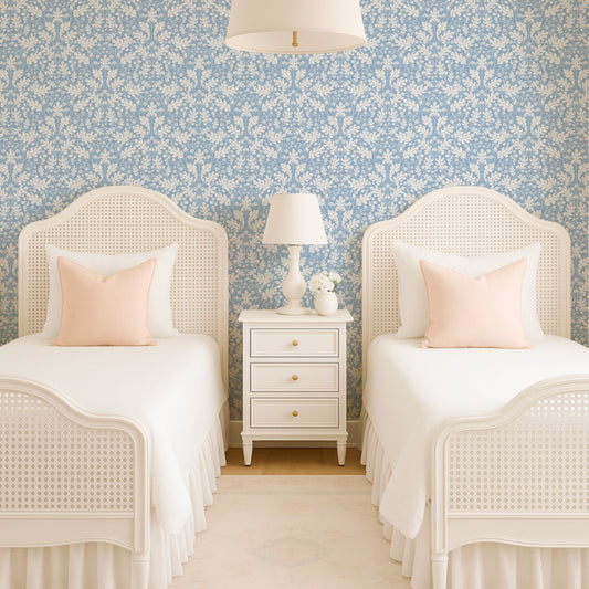 Two white beds with pink pillows in a room with floral wallpaper and a nightstand.