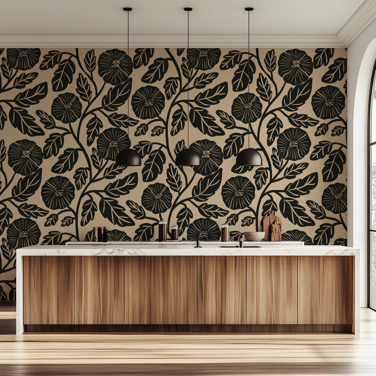 A modern kitchen interior featuring a bold black floral and leaf pattern wallpaper on a warm beige background, paired with a light wood cabinet island and black pendant lights.