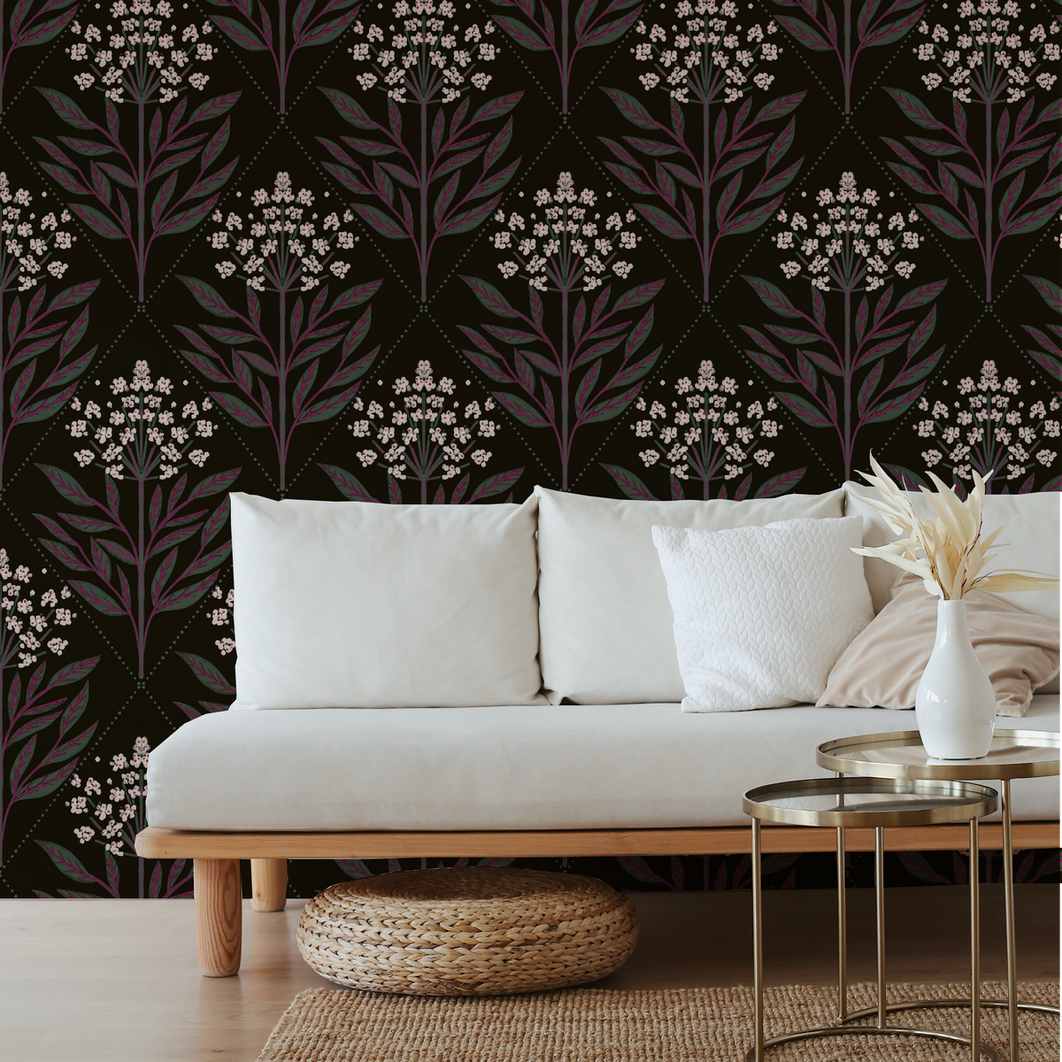 A styled living room scene featuring a dark wallpaper with a repeating botanical damask pattern in muted purple and off-white on a black background, behind a light beige sofa with white and beige pillows.