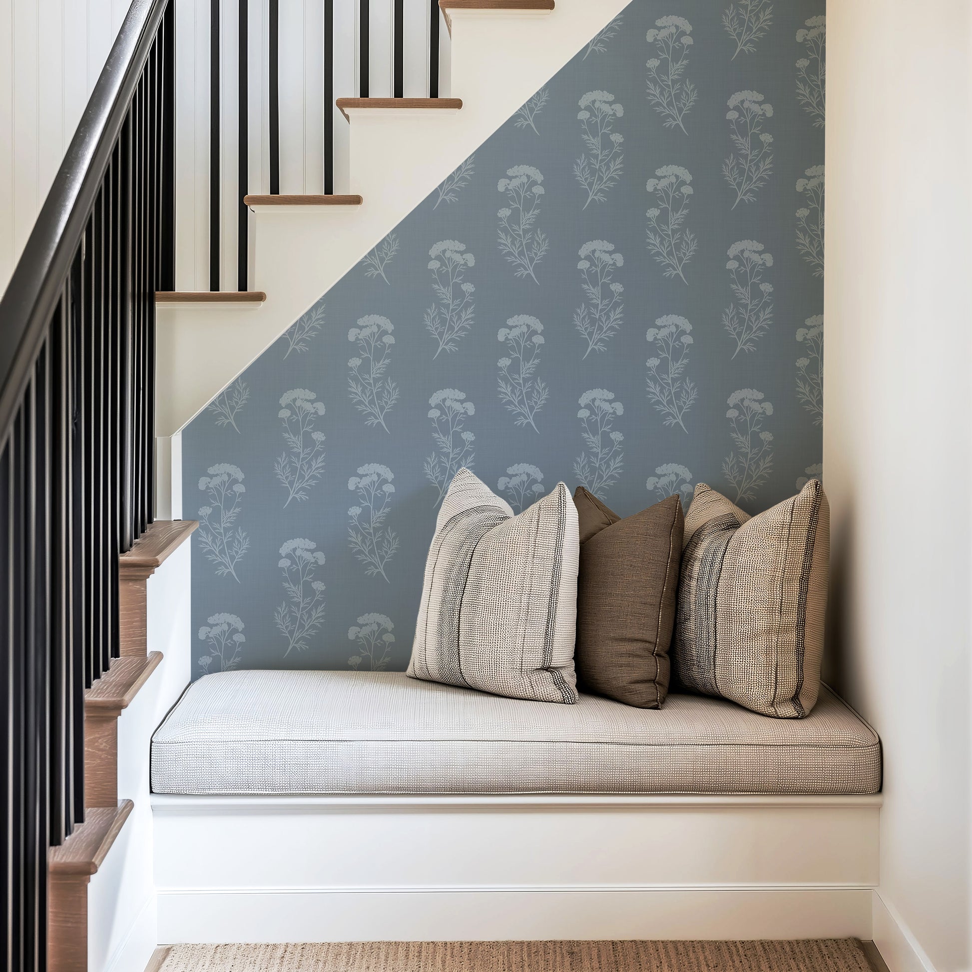 Nook under a staircase with patterned wall, cushioned bench, and decorative pillows.