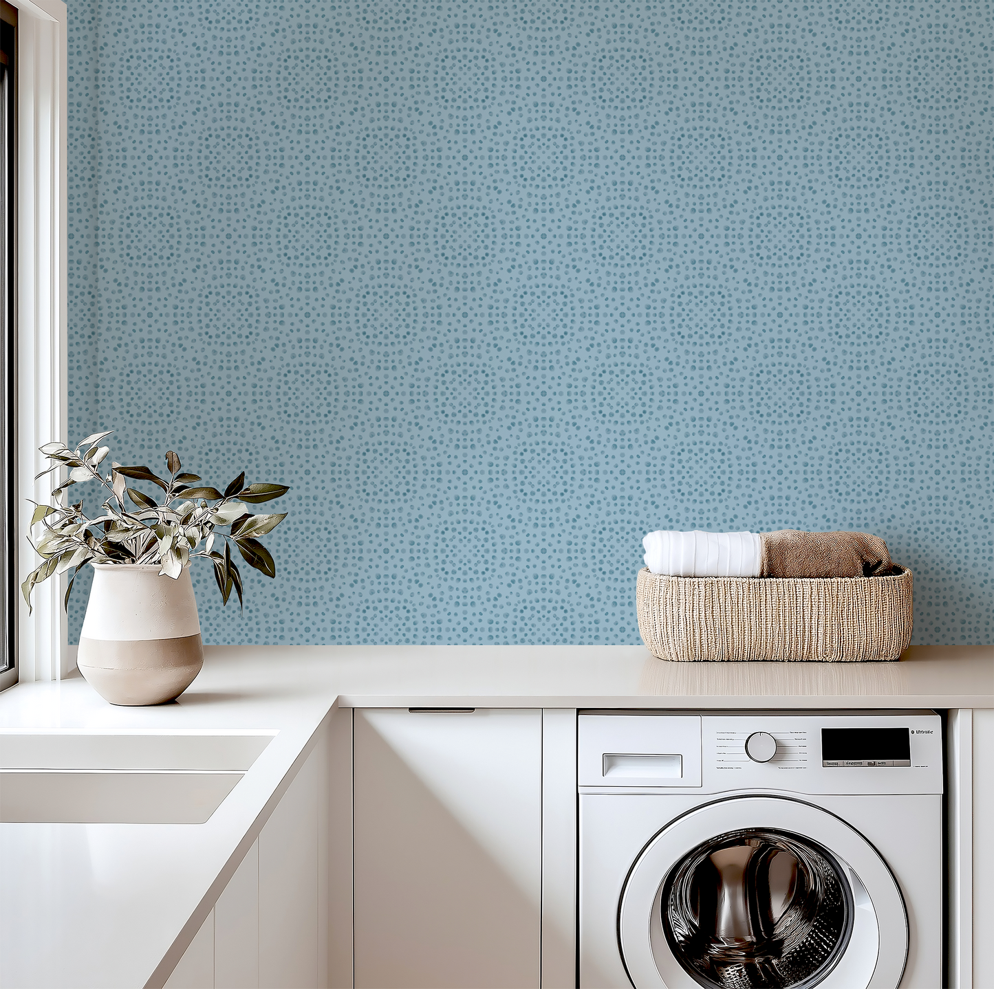 Modern laundry room with washing machine, basket of clothes, and decorative elements against a blue patterned wall.