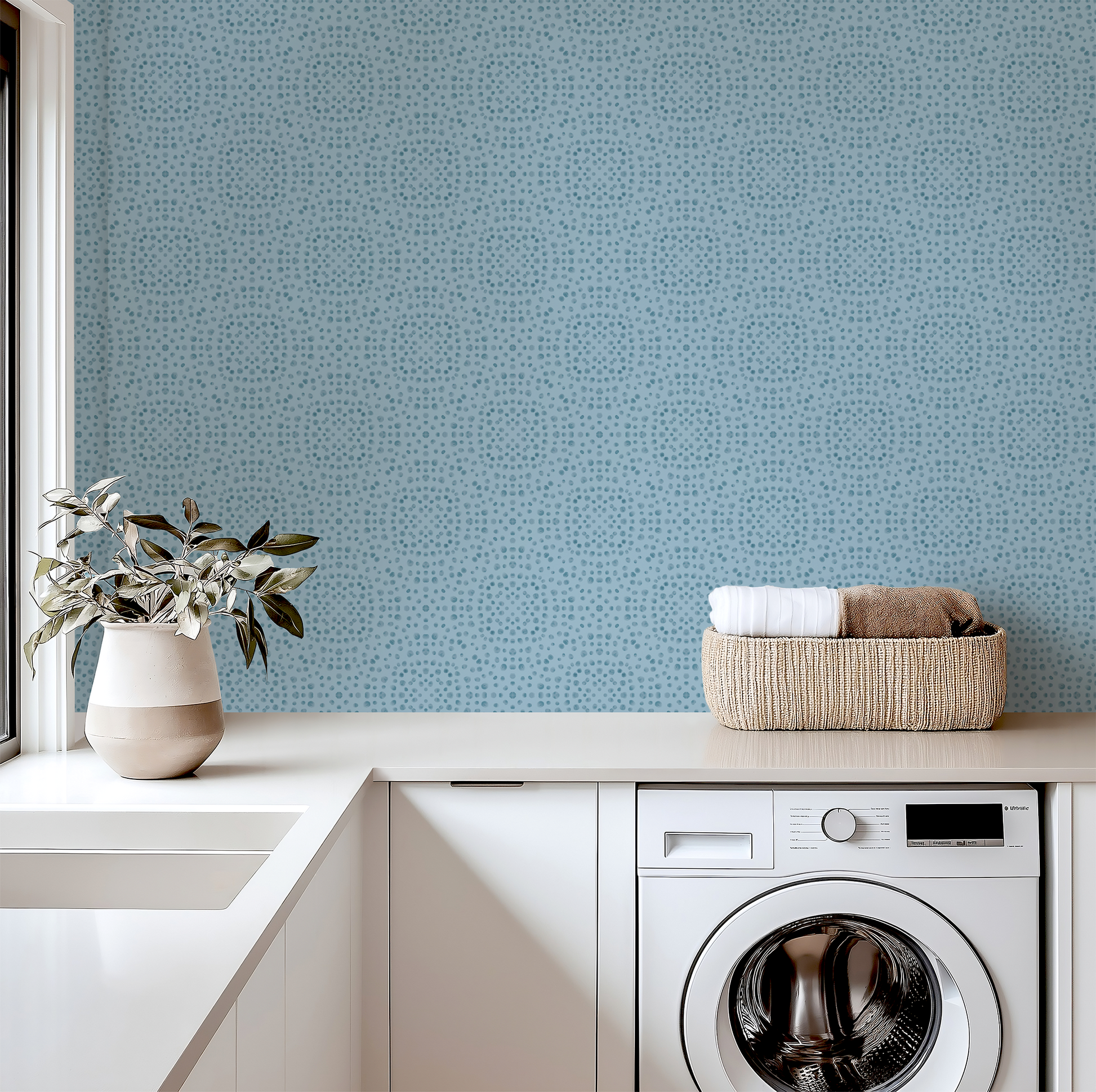 Modern laundry room with washing machine, basket of clothes, and decorative elements against a blue patterned wall.