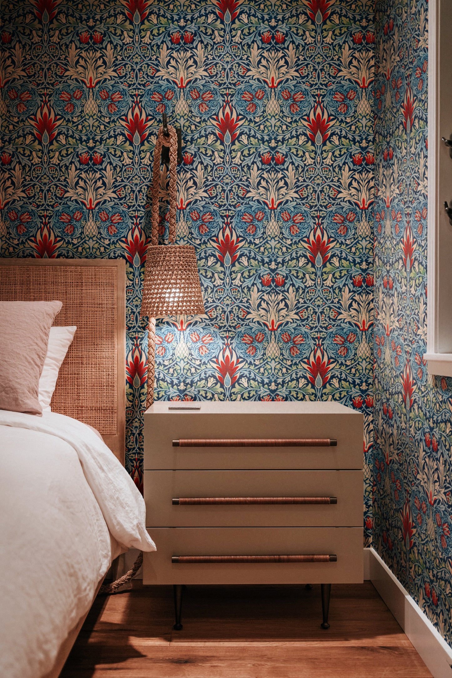 Bedroom with floral wallpaper, wooden bed, and chest of drawers.