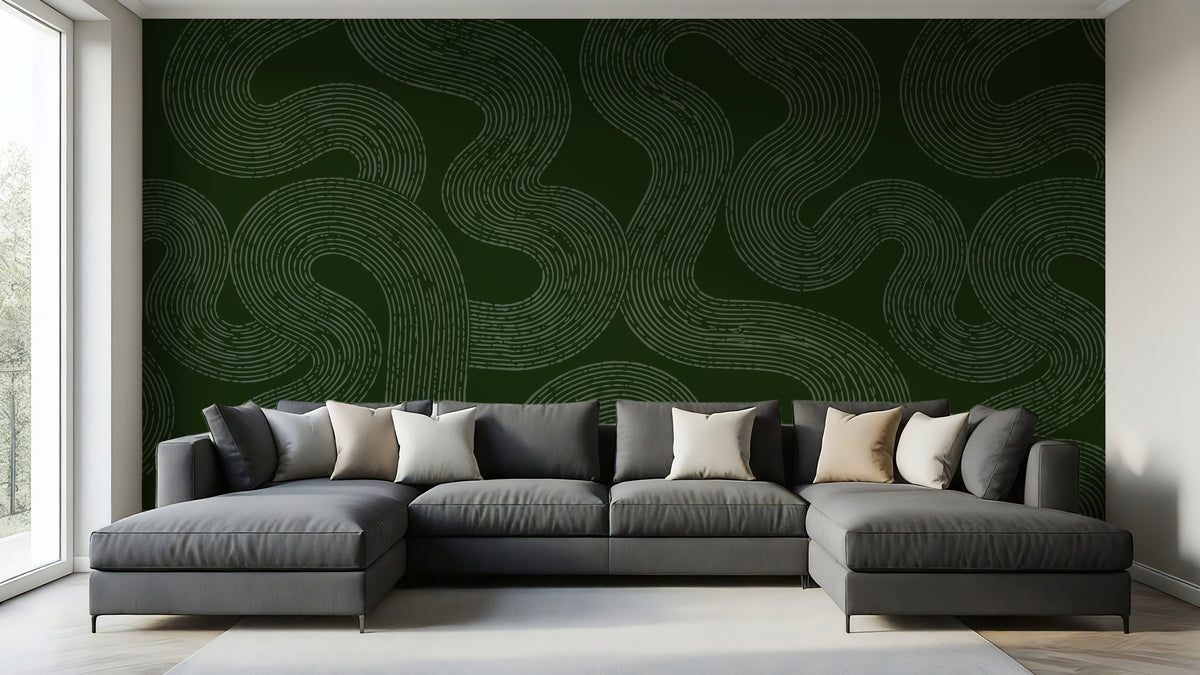 A modern gray sectional sofa with multiple throw pillows is positioned in front of a large dark green accent wall featuring a light beige wavy line pattern. The room has light wood floors and a white window frame on the left.