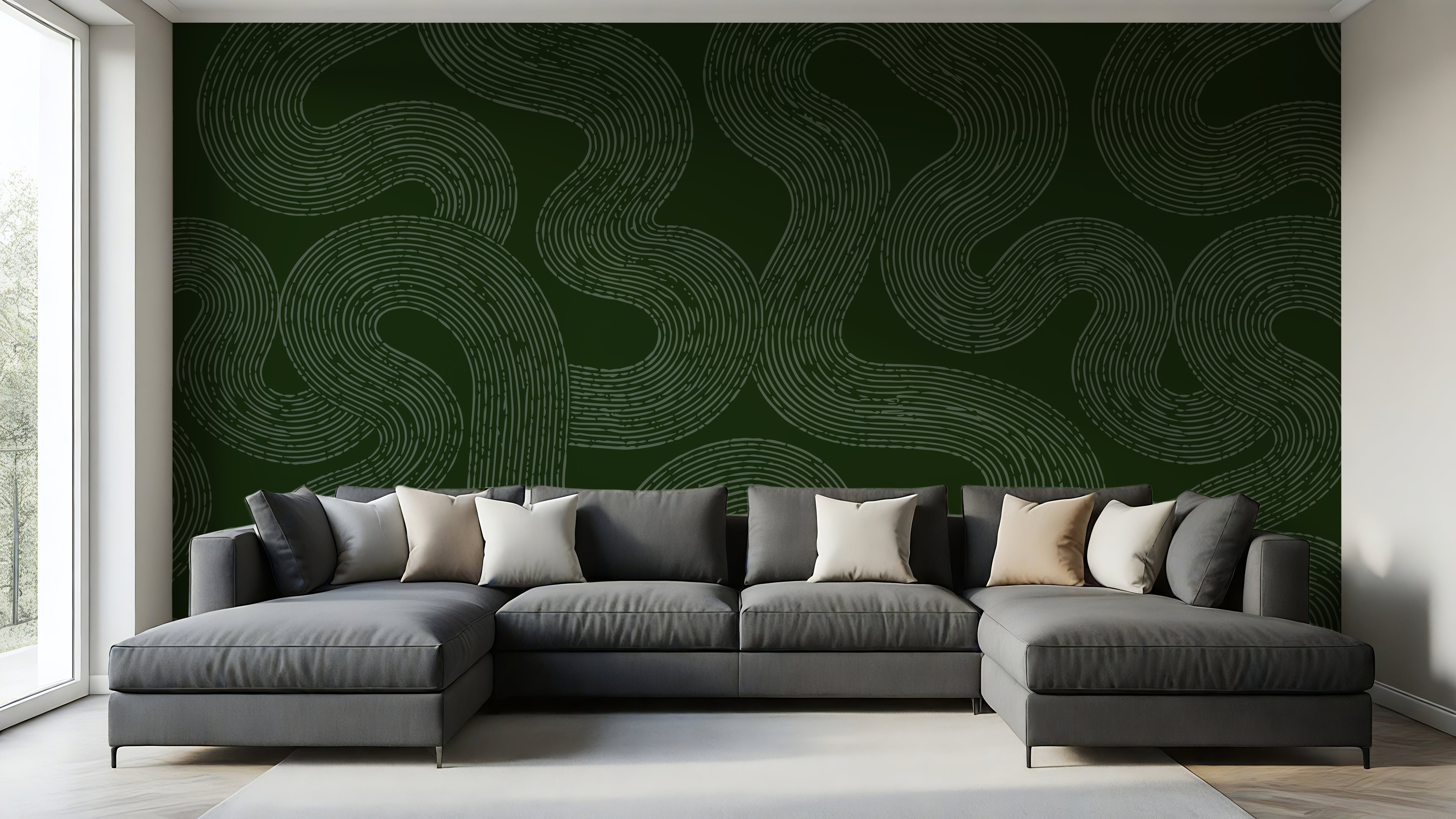 A modern gray sectional sofa with multiple throw pillows is positioned in front of a large dark green accent wall featuring a light beige wavy line pattern. The room has light wood floors and a white window frame on the left.