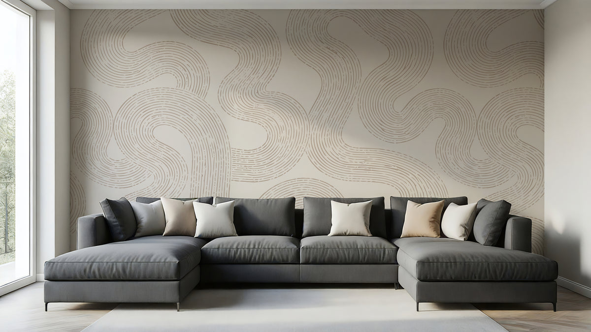 A modern L-shaped sectional sofa in dark gray with beige and white accent pillows, set against a wall with a large beige abstract wavy patterned wallpaper in a bright, contemporary living room.