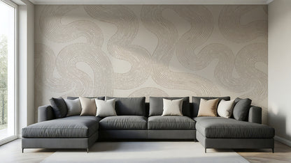 A modern L-shaped sectional sofa in dark gray with beige and white accent pillows, set against a wall with a large beige abstract wavy patterned wallpaper in a bright, contemporary living room.
