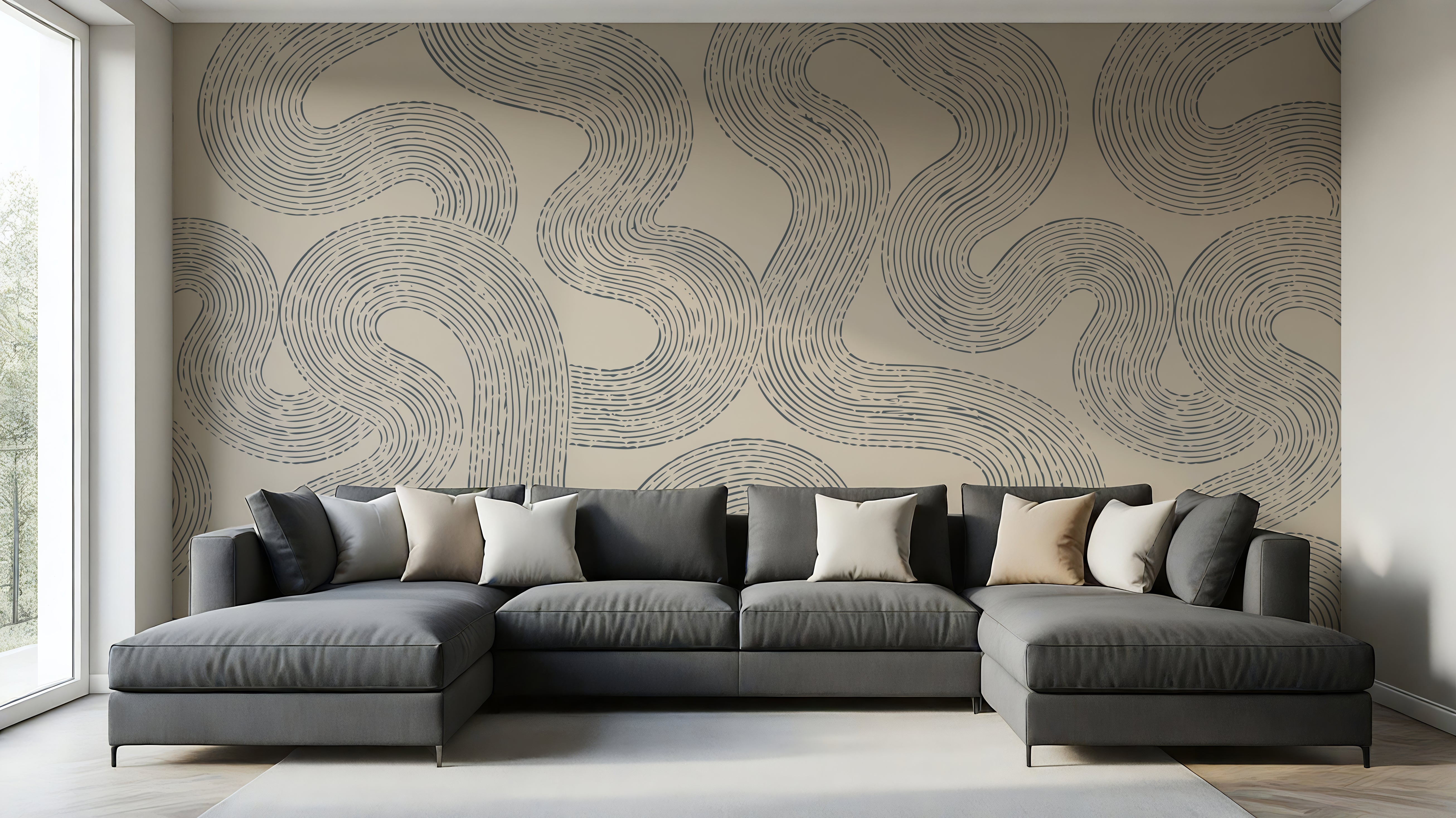 A modern gray sectional sofa with multiple throw pillows is positioned in front of a large wall covered in a beige wallpaper mural with a dark gray wavy line pattern. The room has light wood floors, a white window frame on the left, and a light gray rug on the floor.