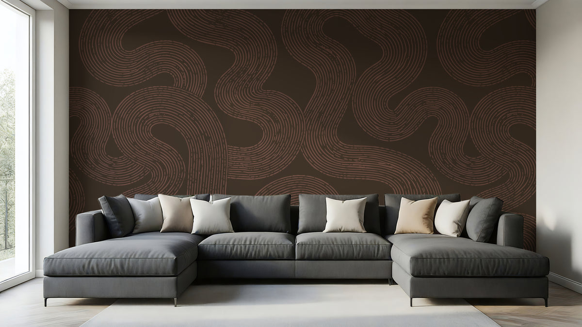 A modern gray sectional sofa with multiple throw pillows is positioned in front of a large wall mural featuring a dark brown background with wavy, flowing tan lines. The room has light-colored walls, a light gray rug, and a window on the left side.