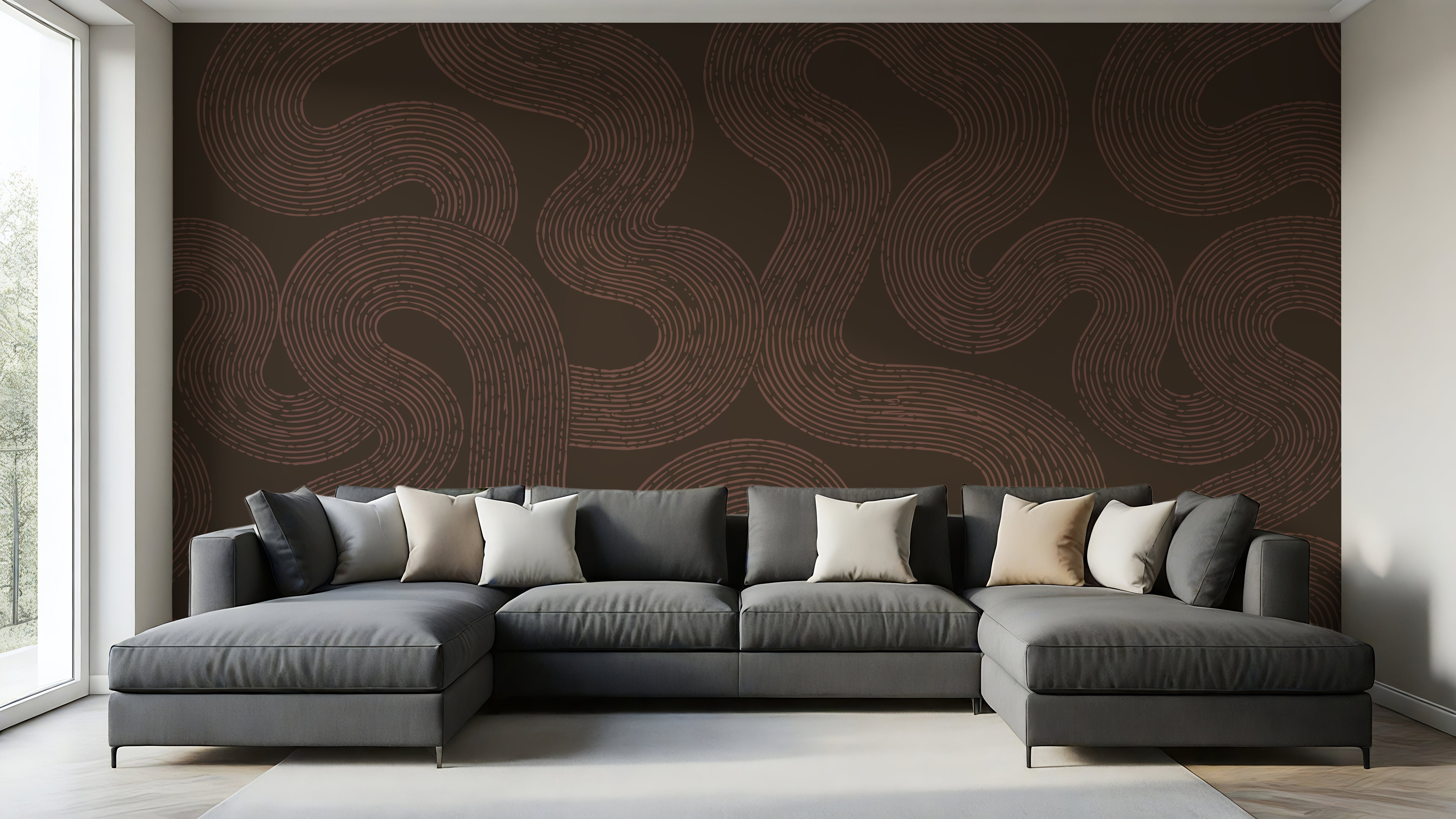 A modern gray sectional sofa with multiple throw pillows is positioned in front of a large wall mural featuring a dark brown background with wavy, flowing tan lines. The room has light-colored walls, a light gray rug, and a window on the left side.