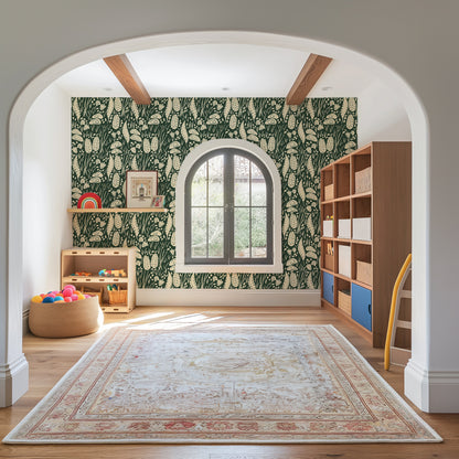 A styled children's playroom viewed through a white arched doorway, featuring dark green and cream botanical patterned wallpaper, a large beige area rug, a window, wooden shelves, and a tan beanbag.